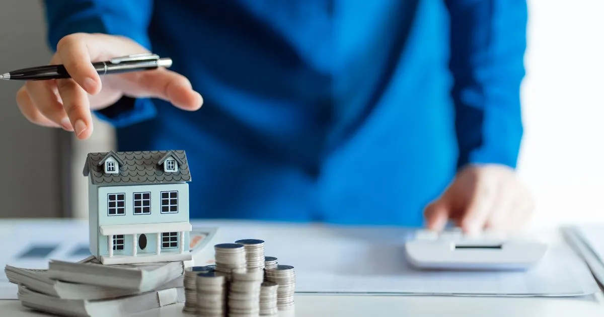 Článek Financování nemovitosti od A do Z Finanční poradce ukazuje na model domu stojící na hromádkách bankovek a mincí