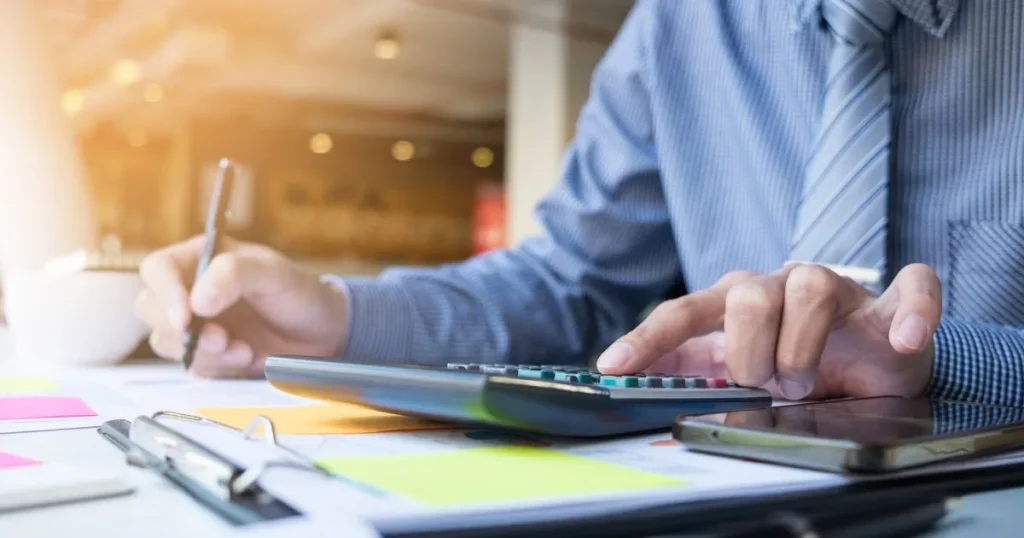 Detail rukou finančního poradce, který počítá na kalkulačce a zapisuje si poznámky