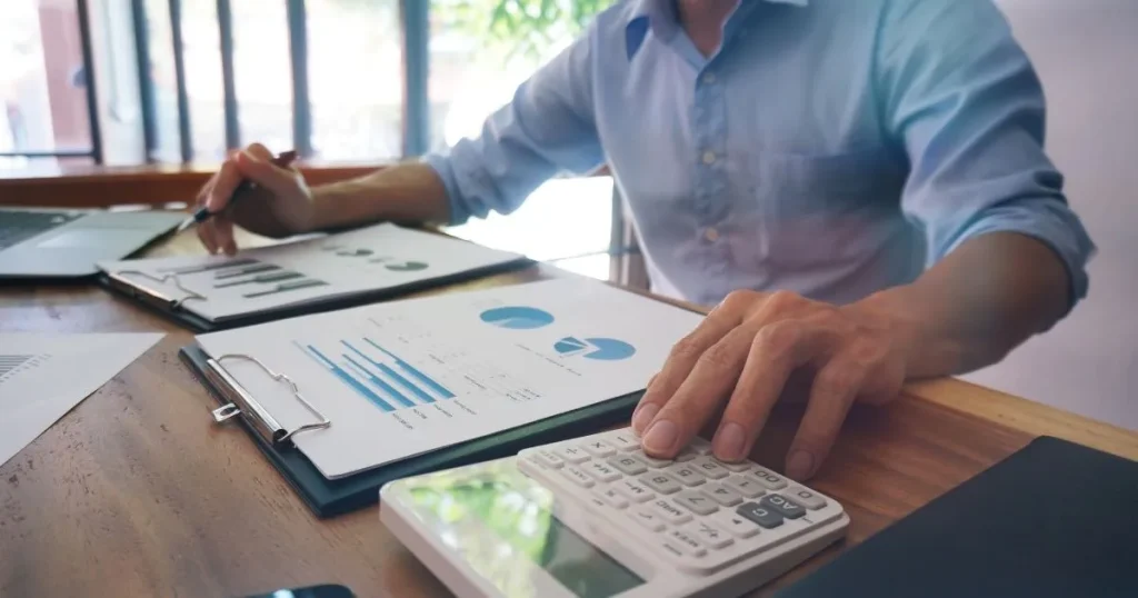 Detail rukou při finančních výpočtech na bílé kalkulačce nad tištěnými grafy a statistikami